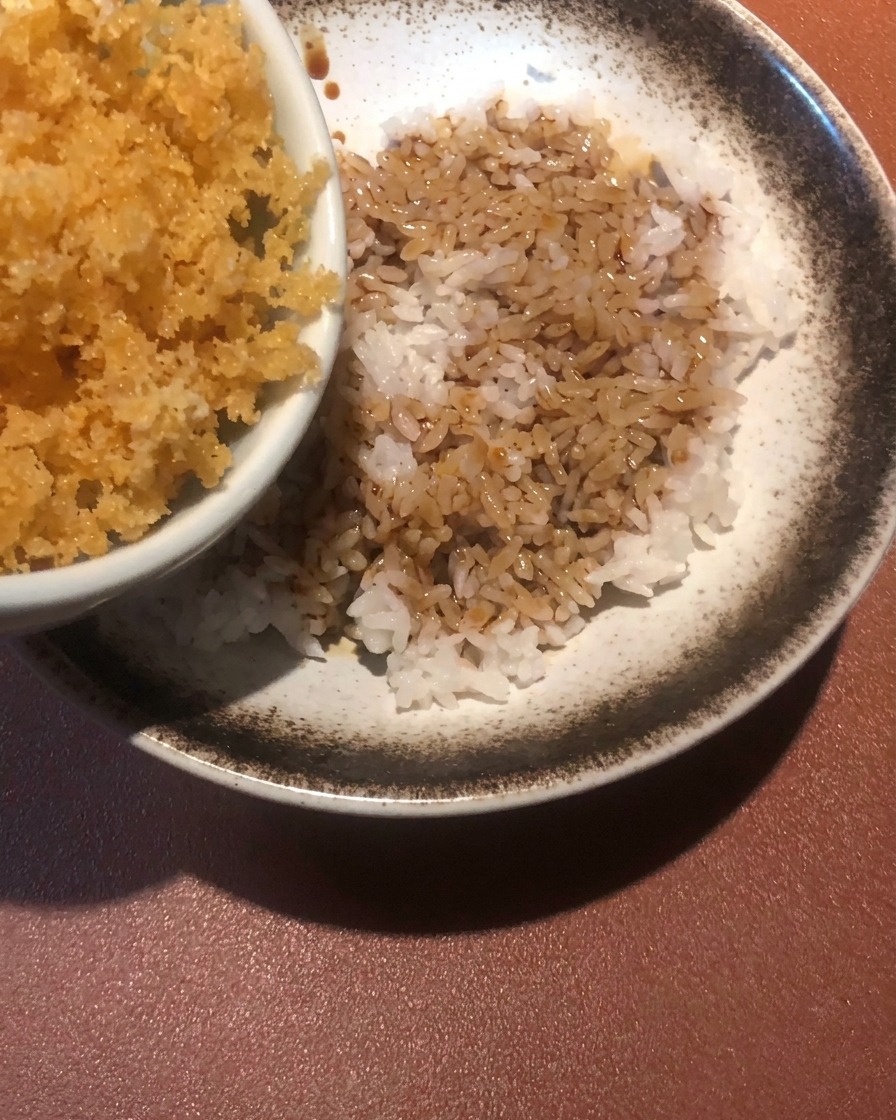 Migas de masa frita doradas siendo esparcidas sobre un cuenco de arroz con salsa.