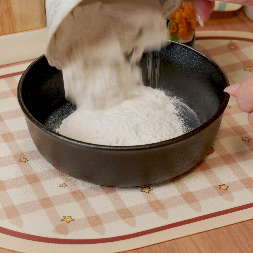 Un batidor mezclando harina para tempura y agua en una masa suave y fina en un bol oscuro.