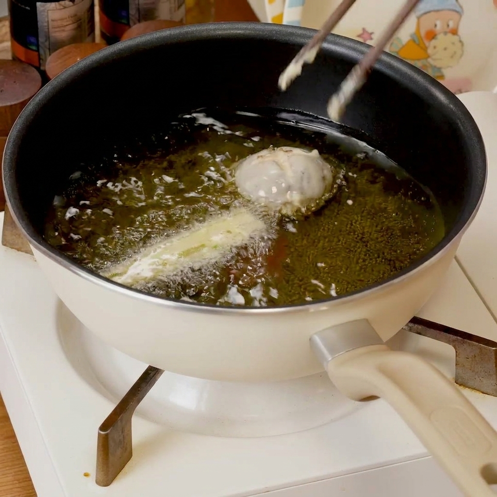 Piezas de tempura rebozadas chisporroteando en una sartén poco profunda con aceite caliente, volviéndose doradas.