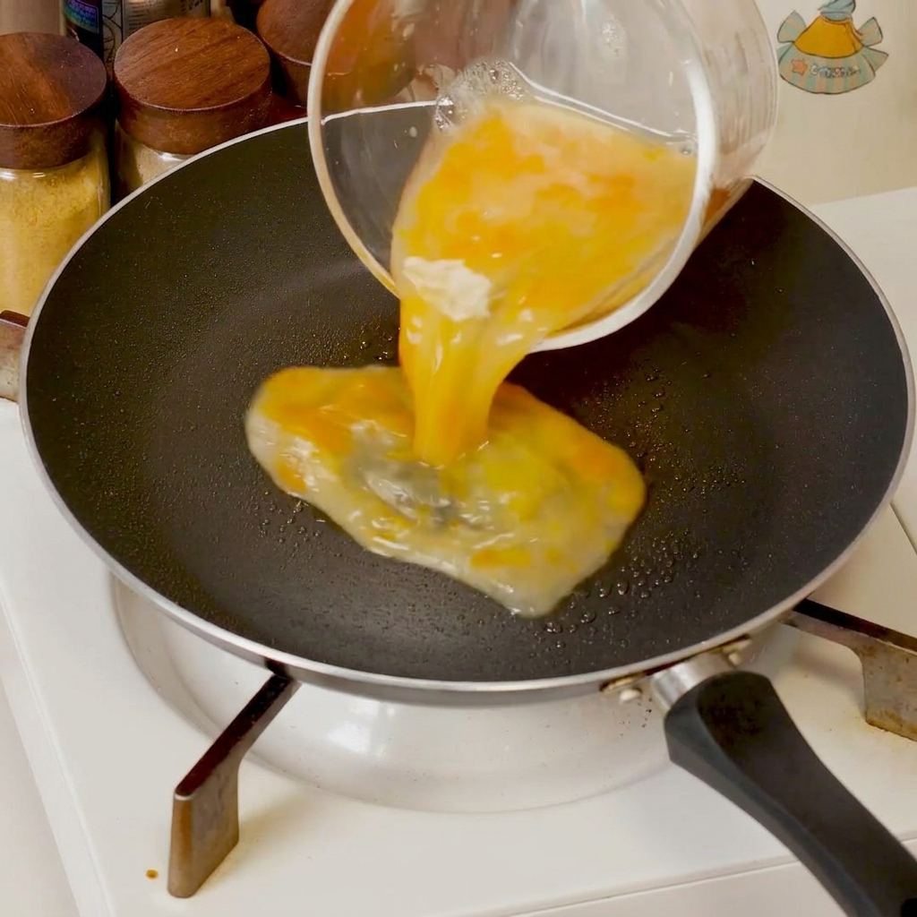 Huevos batidos cocinándose en una sartén, siendo empujados hacia el centro con una espátula para formar cuajadas suaves.