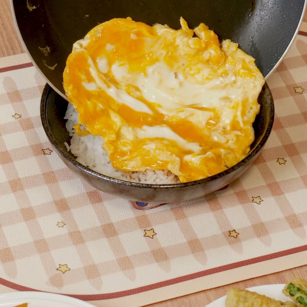 Huevos revueltos suaves con salsa siendo deslizados sobre un tazón de arroz blanco.