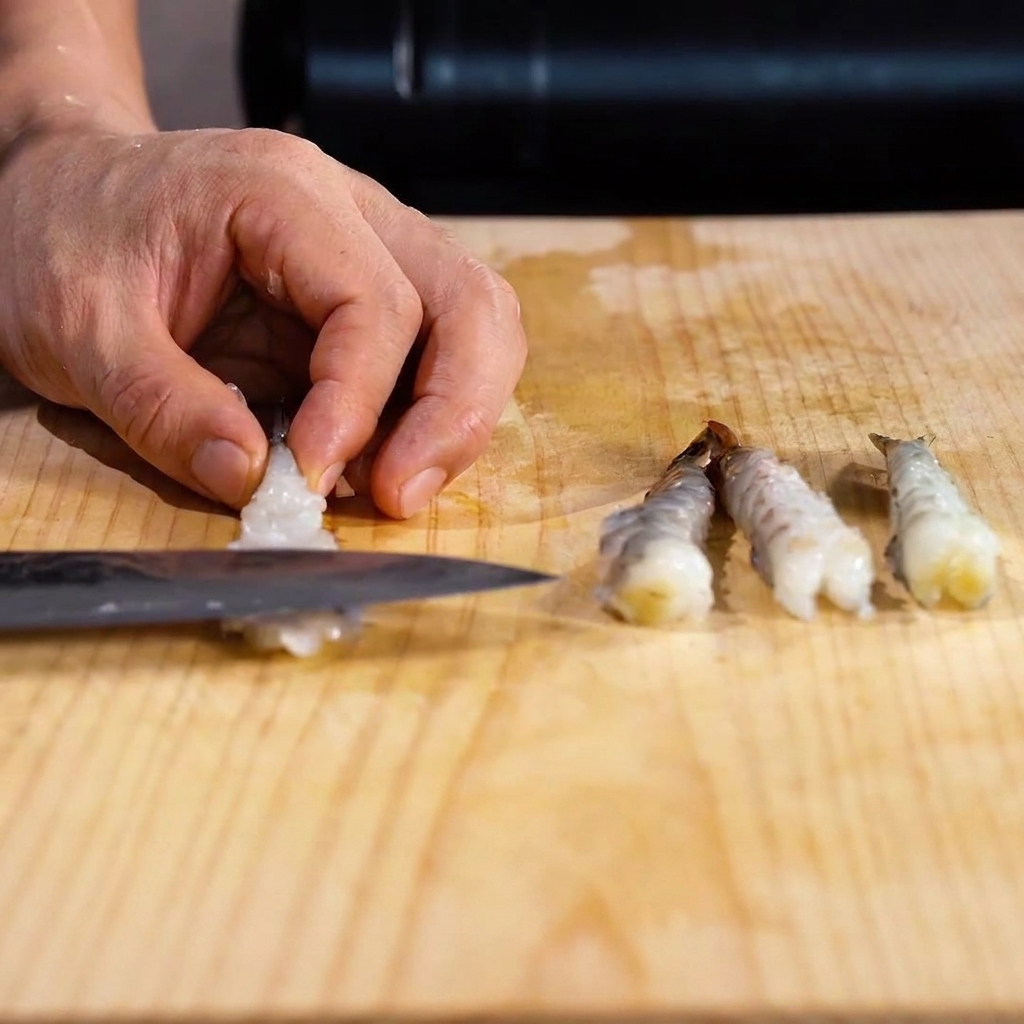 El lomo de un cuchillo presionando el vientre del camarón para aplanarlo.