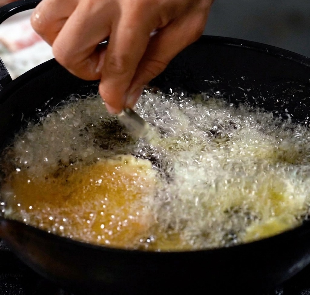 Camarones friéndose en una olla profunda con aceite caliente, creando una capa dorada y crujiente.