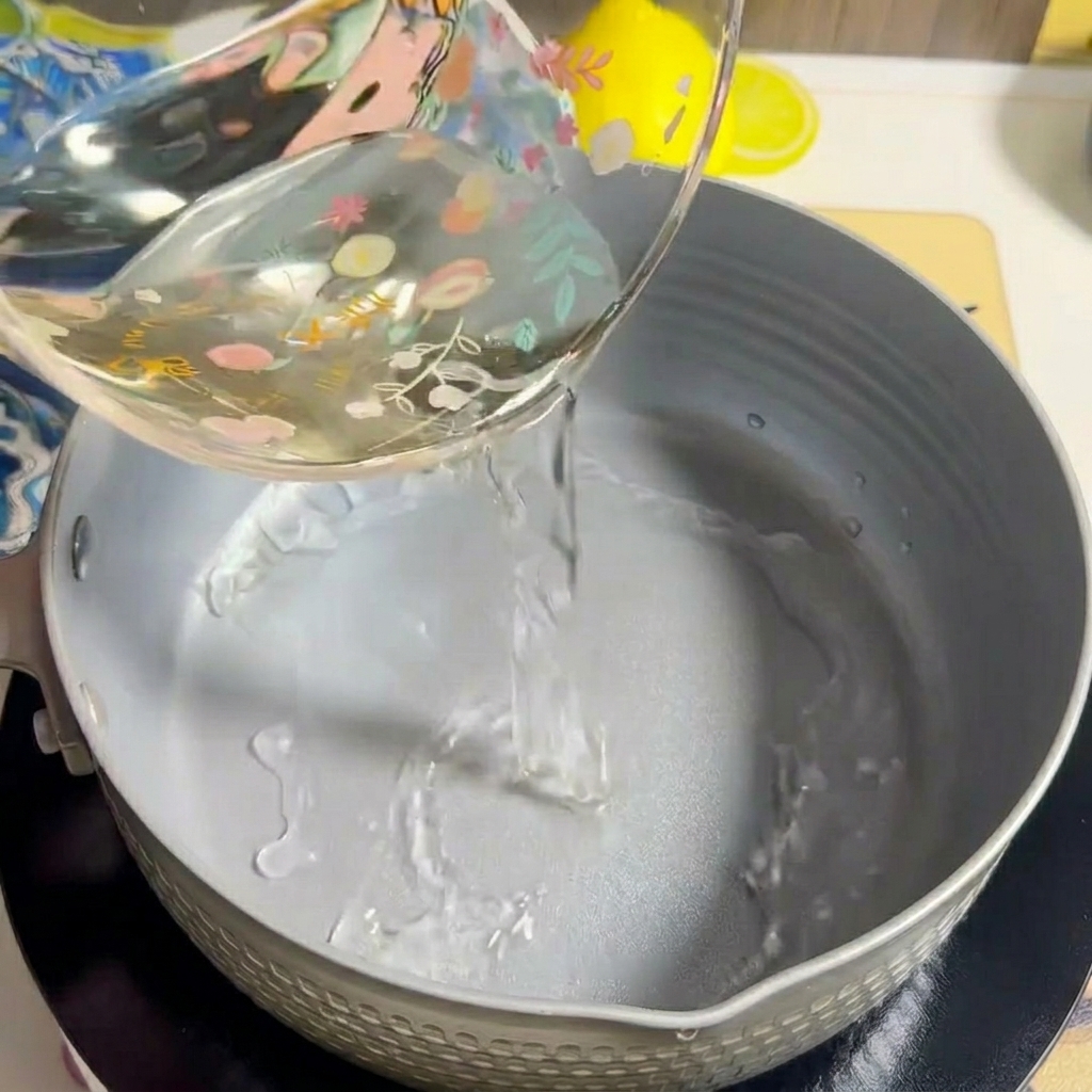 Agua siendo vertida en una olla de cocina gris vacía sobre una estufa.