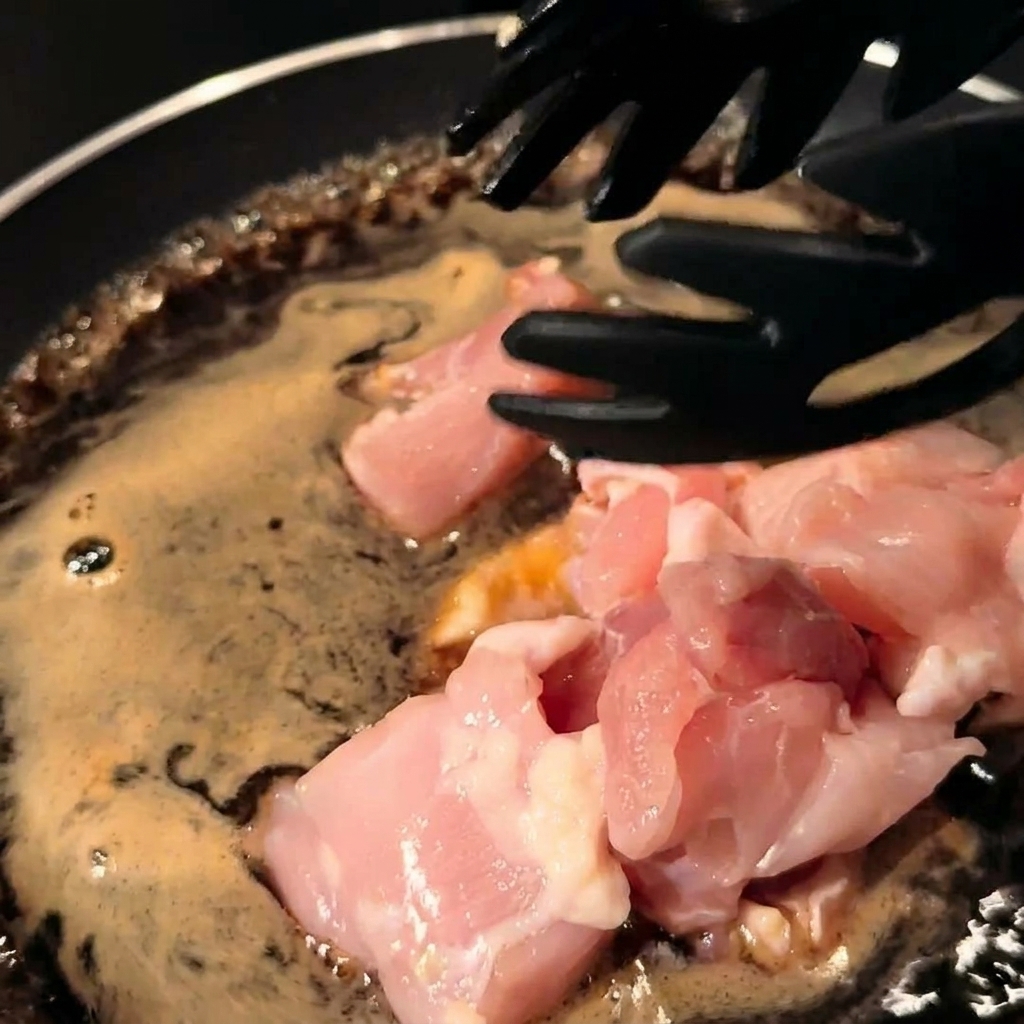 Trozos de pollo y láminas de cebolla mezclándose con la salsa en la sartén.