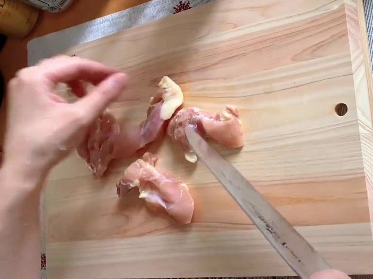 Contramuslo de pollo siendo recortado y cortado en trozos sobre una tabla de cortar.