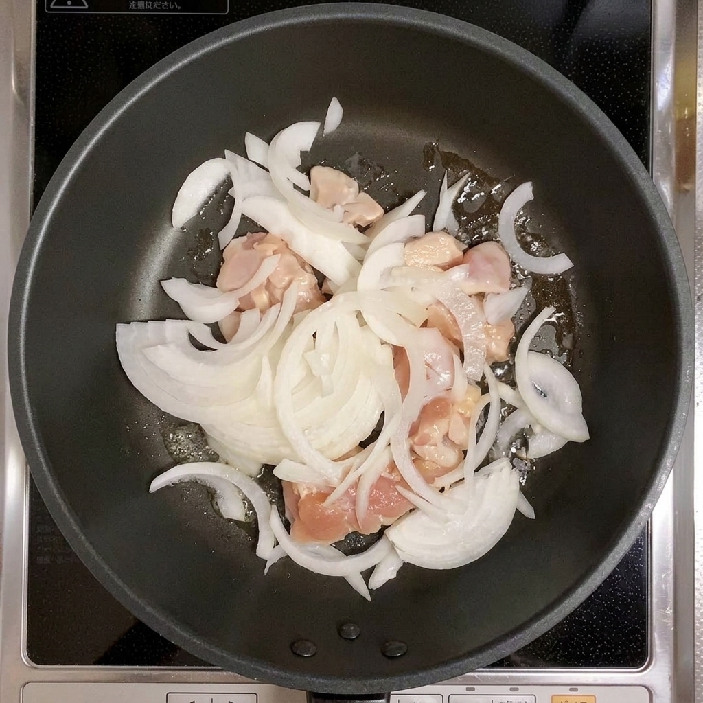 Pollo y cebollas en rodajas siendo mezclados en una sartén.