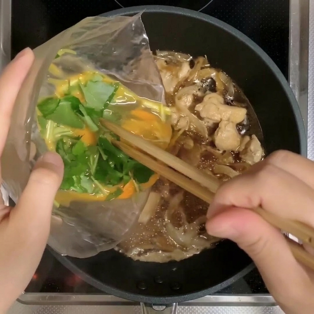 Dos tercios de la mezcla de huevo y mitsuba siendo vertidos en la sartén con pollo y cebollas.