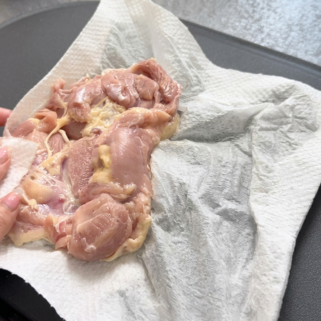 Uso de pinzas para colocar suavemente un muslo de pollo crudo en una sartén caliente.