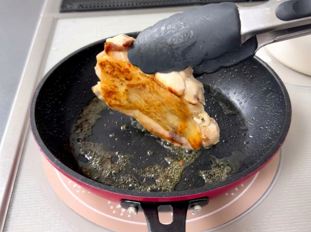 Pinzas volteando una pieza de pollo revelando una piel perfectamente dorada y crujiente.