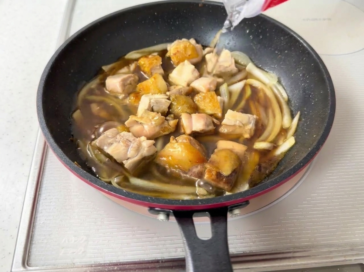 Agua siendo vertida en la sartén con el pollo y la salsa.