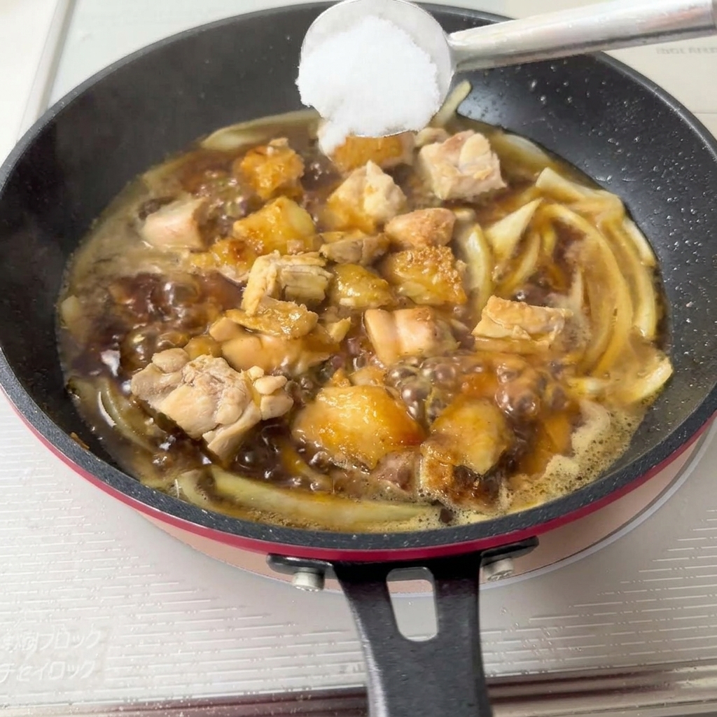 Una cuchara añadiendo azúcar a la mezcla de pollo y cebolla.