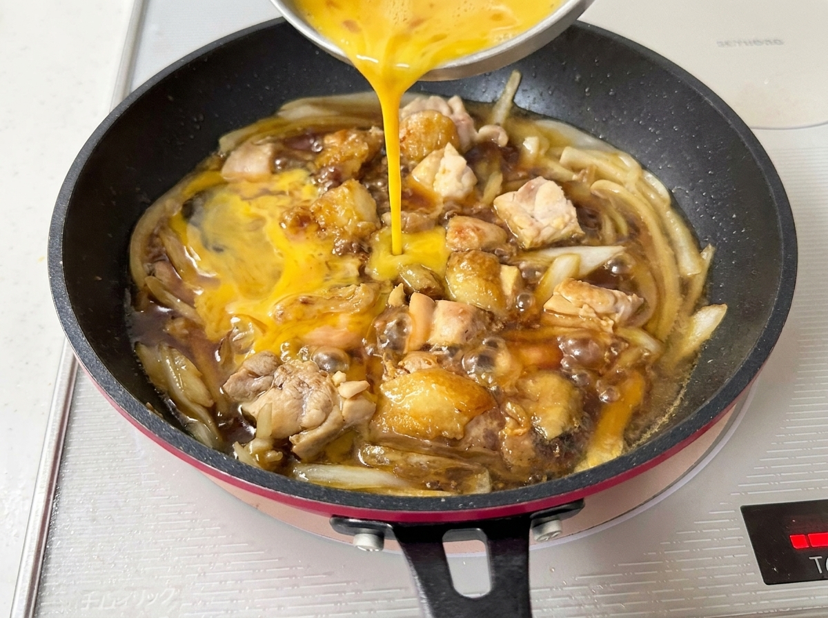 Huevos batidos vertiéndose sobre el pollo y la cebolla en la sartén.