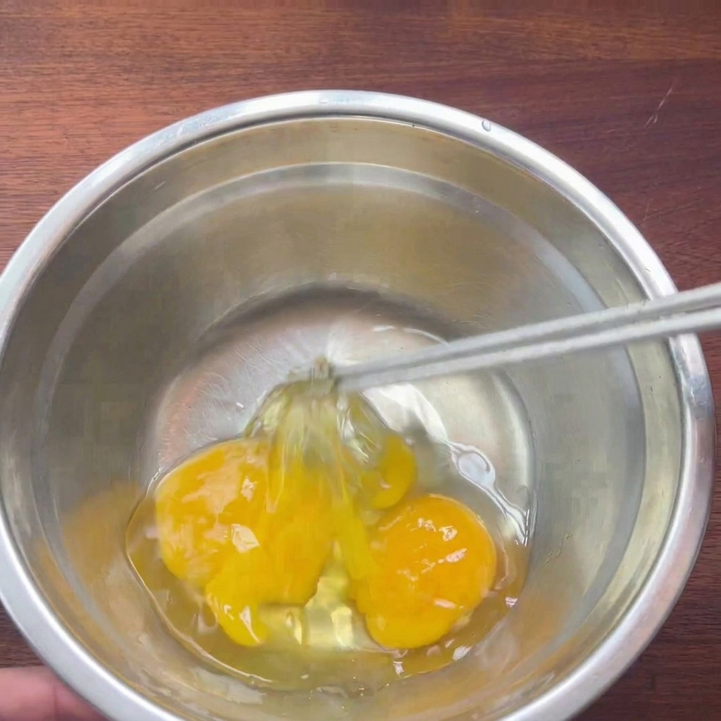 Dos huevos crudos en un cuenco de metal siendo batidos suavemente con palillos.