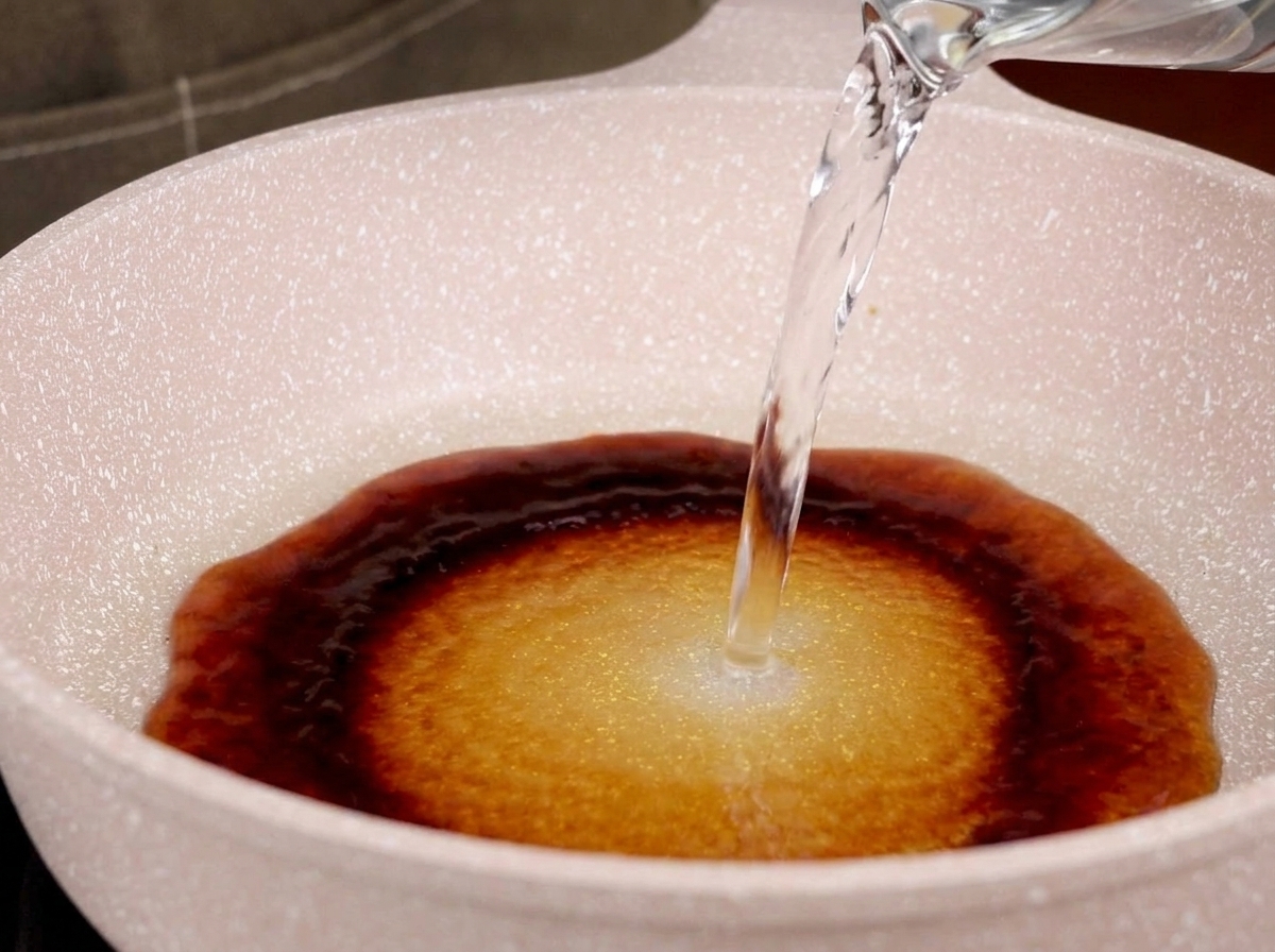 Agua vertiéndose en una sartén con salsa teriyaki, formando una mezcla.