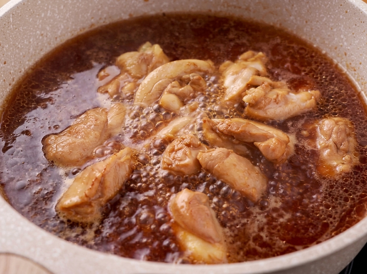 Espuma siendo retirada de la superficie de una mezcla hirviendo de pollo y salsa teriyaki.