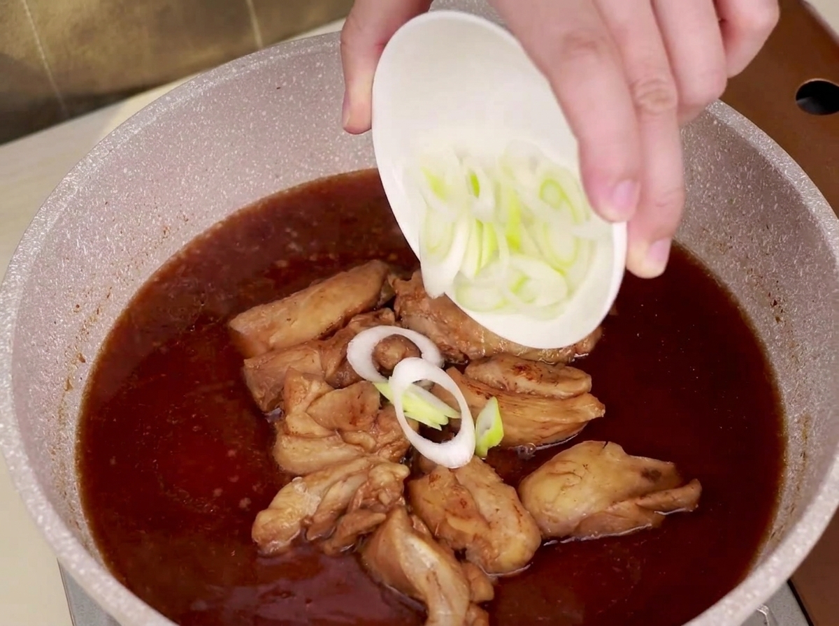 Puerro en rodajas espolvoreándose en una sartén con pollo a fuego lento y salsa teriyaki.