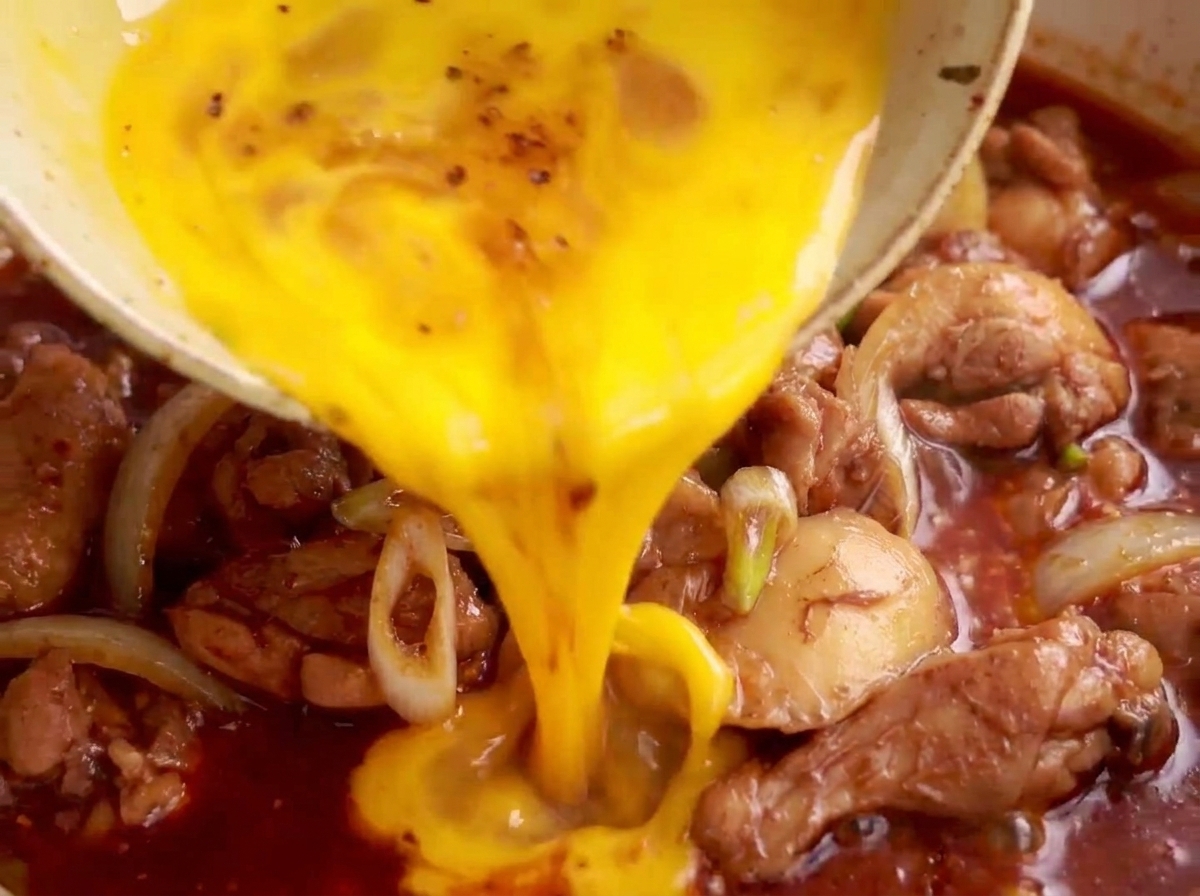 Mezcla de huevo batido vertiéndose sobre el pollo y los puerros a fuego lento en una sartén.
