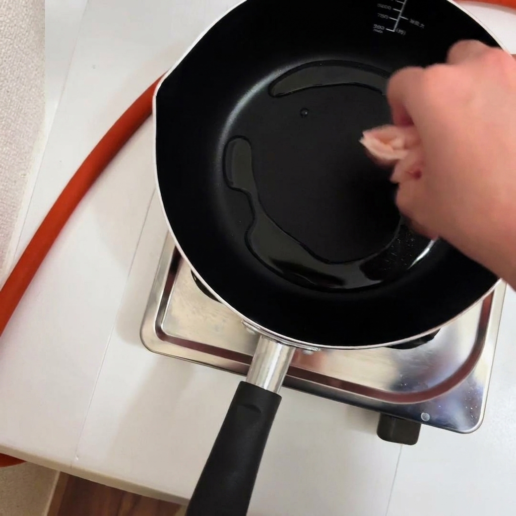 Trozos de pollo siendo añadidos a una sartén con aceite caliente.