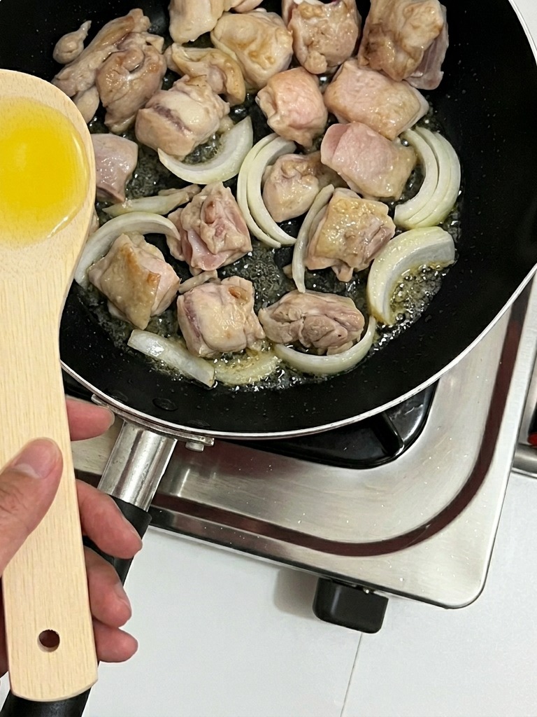 Tiras de cebolla siendo removidas en la sartén con los trozos de pollo.