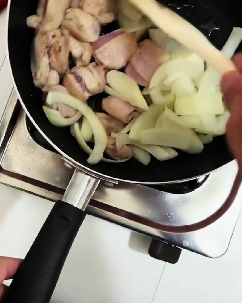 Vino de cocina siendo vertido desde un cucharón en la sartén con pollo y cebollas.