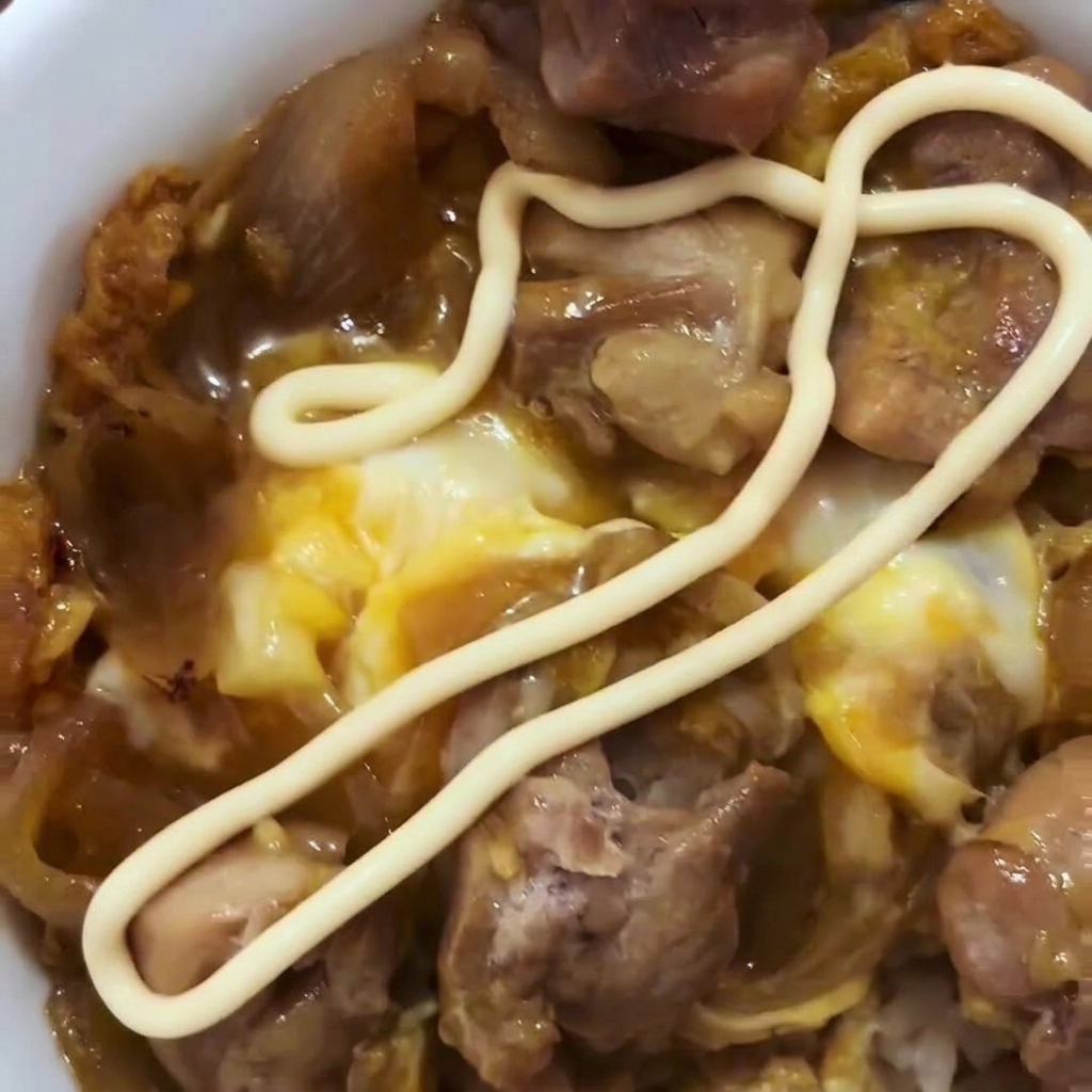 Huevos batidos siendo vertidos sobre el pollo y la cebolla cocinados en una sartén.