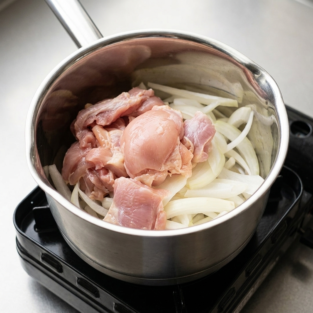 Cebollas y trozos de pollo en una olla siendo aderezados con los condimentos líquidos.