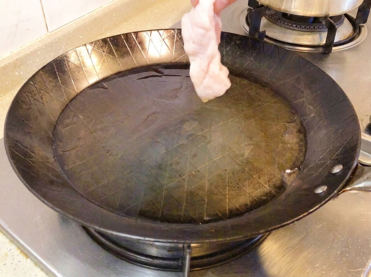 Muslo de pollo crudo con la piel hacia abajo en una sartén caliente.