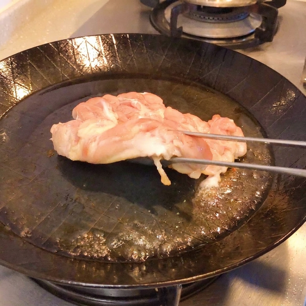 Unas pinzas levantando el pollo en la sartén para mostrar la piel dorada y crujiente.