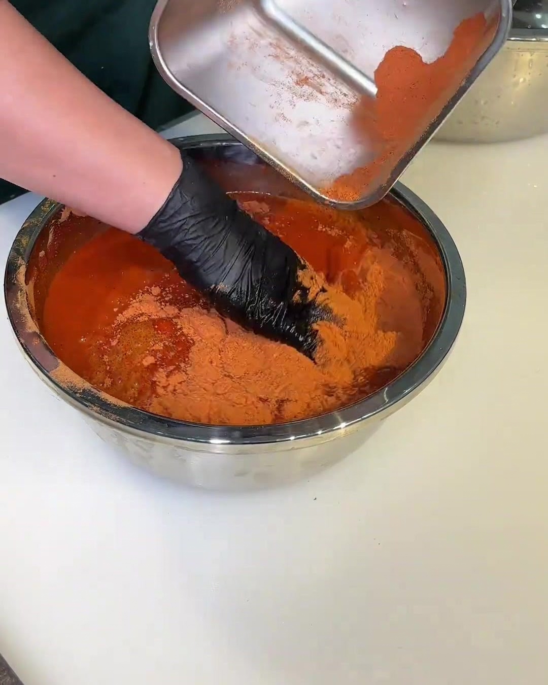 Un bol lleno de adobo rojo con una mano enguantada removiendo las rebanadas de cerdo para cubrirlas uniformemente.