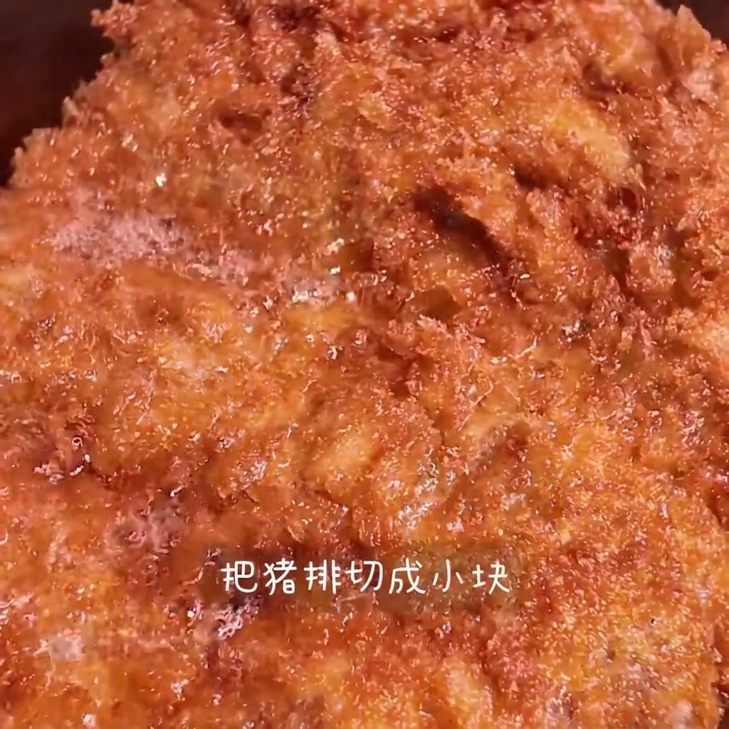 Una chuleta de cerdo frita dorada siendo cortada en tiras sobre una tabla de madera.