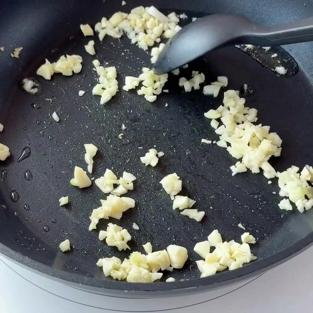 Ajo picado y cebolla roja cocinándose en una sartén antiadherente oscura.