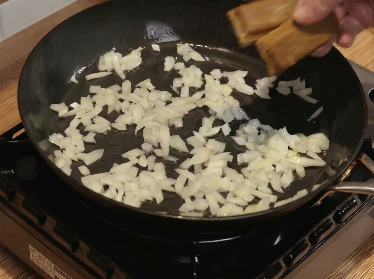 Bloques de curry y agua mezclándose con cebollas salteadas en una sartén.
