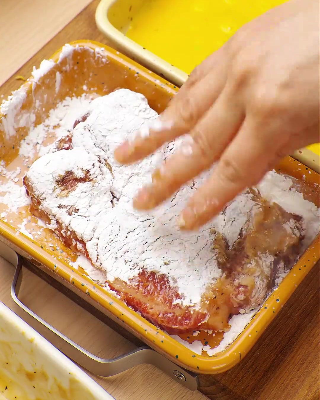 Una mano presionando una chuleta de cerdo cubierta de huevo en una bandeja con pan rallado panko, asegurando una cobertura total.