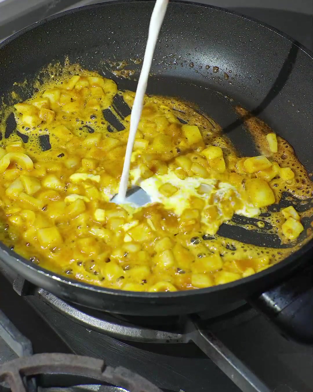 Leche de coco vertiéndose en una sartén con curry derretido y cebollas salteadas, creando una salsa cremosa de color amarillo.