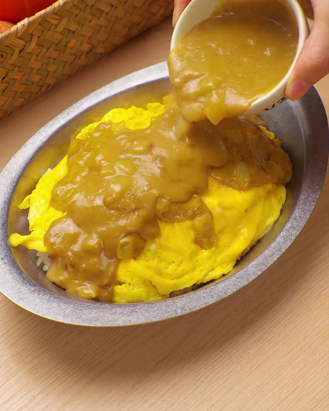 Rica salsa de curry amarilla vertiéndose desde un tazón pequeño sobre una cama de huevos revueltos y arroz.
