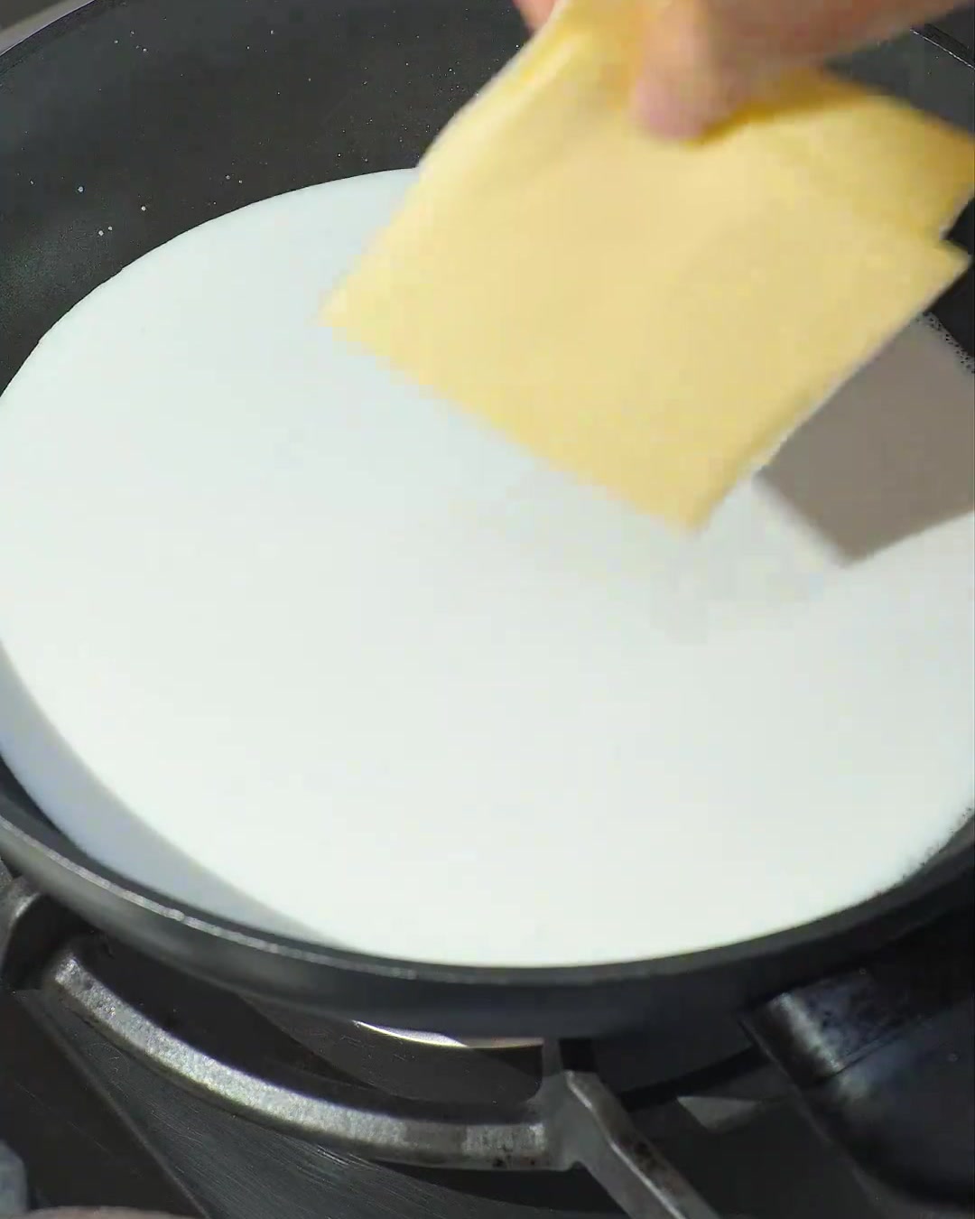 Dos rebanadas de queso amarillo derritiéndose en leche de coco blanca a fuego lento en una sartén oscura.