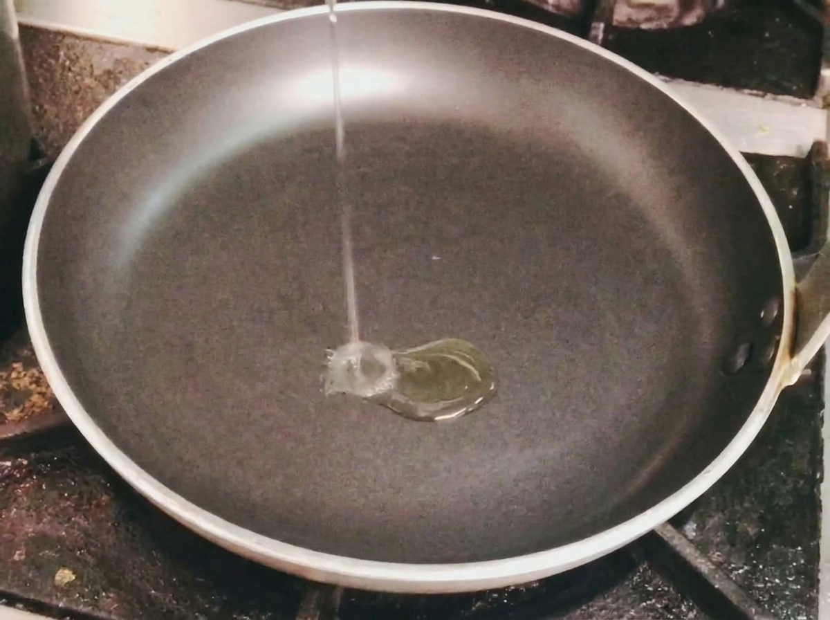 Un fino hilo de aceite de cocina vertiéndose en una sartén negra vacía sobre un fuego.
