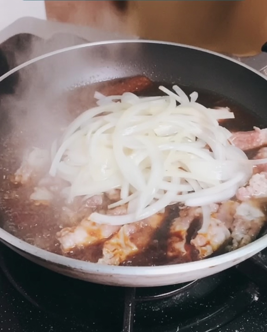 Añadiendo las cebollas previamente cocinadas a la sartén con la ternera a fuego lento.