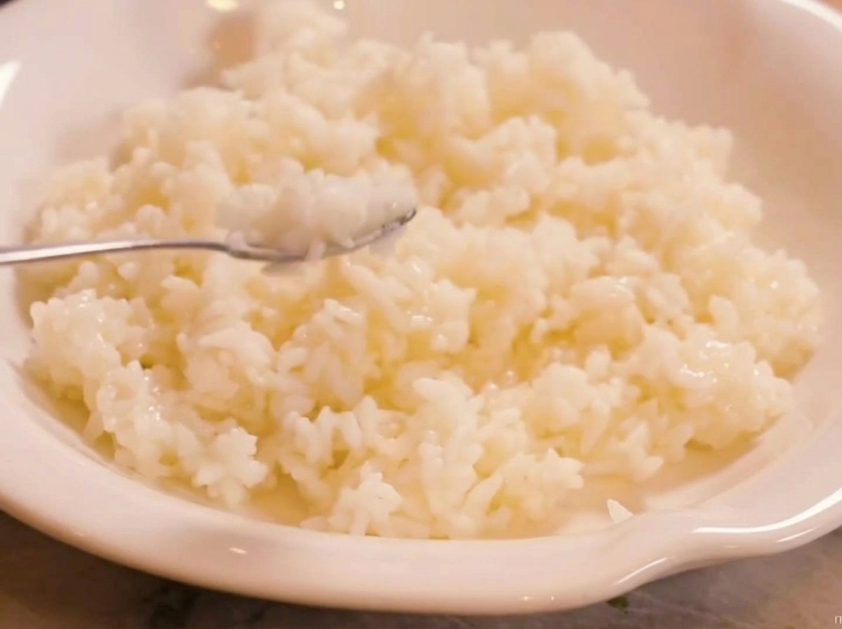 Arroz aromático al vapor siendo mezclado con vinagre de sushi en un bol blanco.