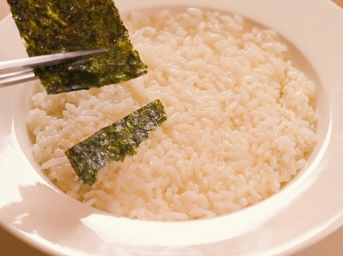 Tiras de alga tostada siendo colocadas sobre el arroz sazonado.