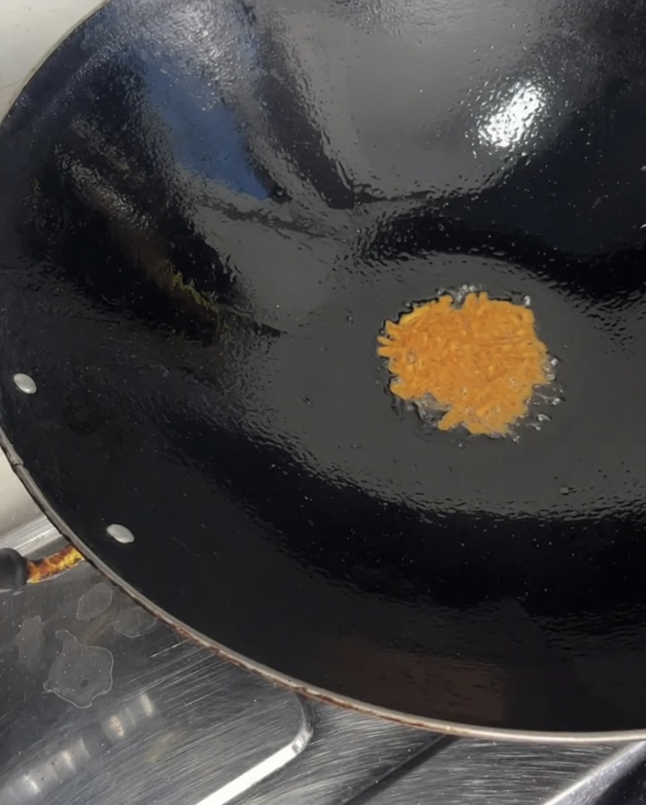 Huevas crudas y anaranjadas de erizo de mar vertidas desde un tazón transparente hacia un wok caliente.