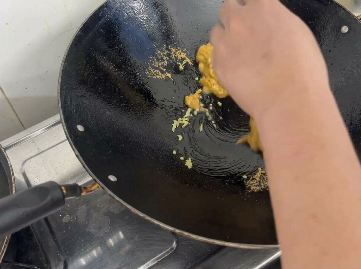 Huevas de erizo de mar cocidas, desmenuzadas y mezcladas con jengibre picado en un wok de metal curado.
