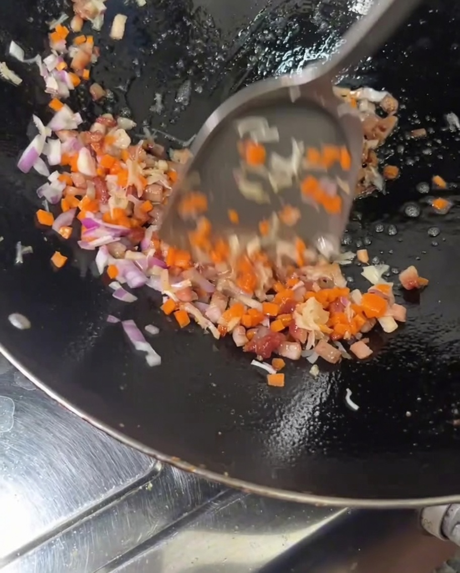 Añadiendo cubitos de zanahorias anaranjadas y cebollas rojas a un wok caliente que contiene carne y vieiras en cocción.
