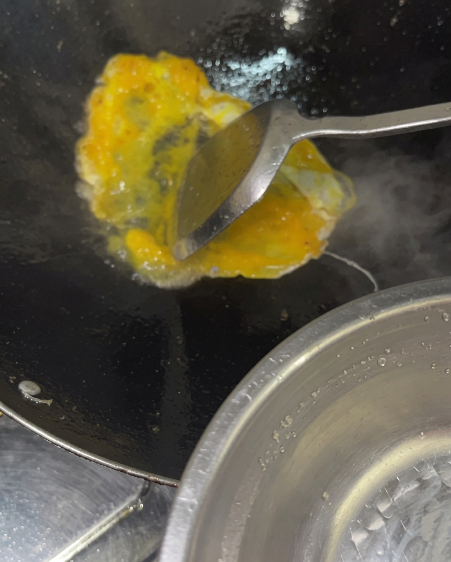 Vertiendo un chorrito de huevos crudos batidos en un wok caliente que contiene vegetales y carnes cocidos.