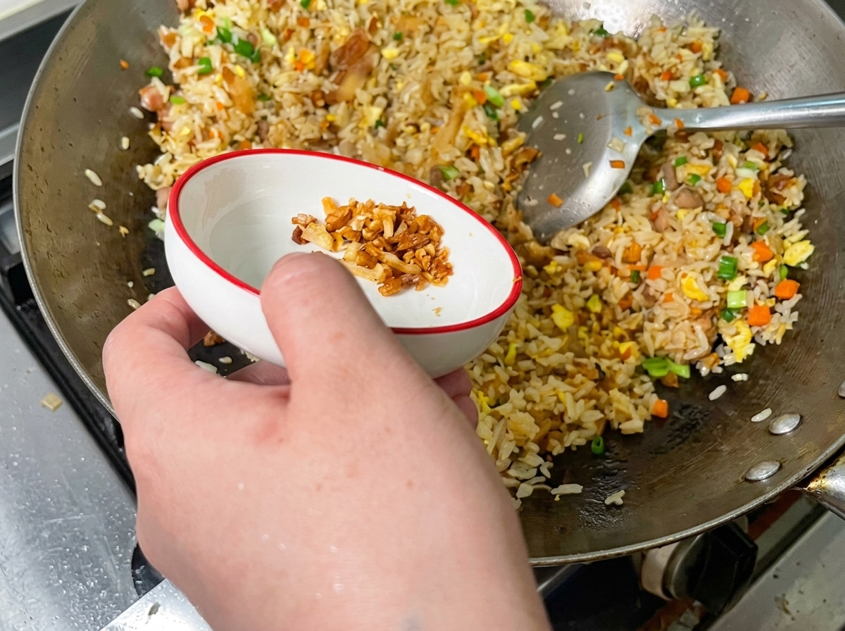 Chicharrones de cerdo crujientes y dorados esparcidos sobre una colorida tanda de arroz frito en un wok.