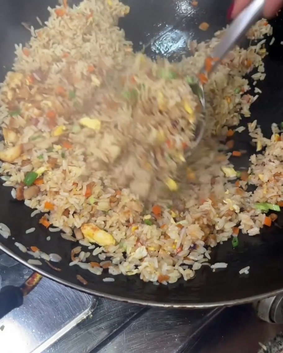 Arroz frito siendo lanzado y mezclado en lo alto de un wok para combinar todos los ingredientes minuciosamente.