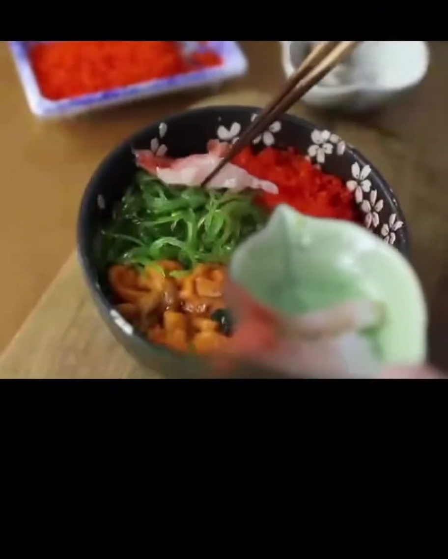 Camarones dulces crudos y translúcidos colocados a un lado de un tazón de arroz con mariscos.