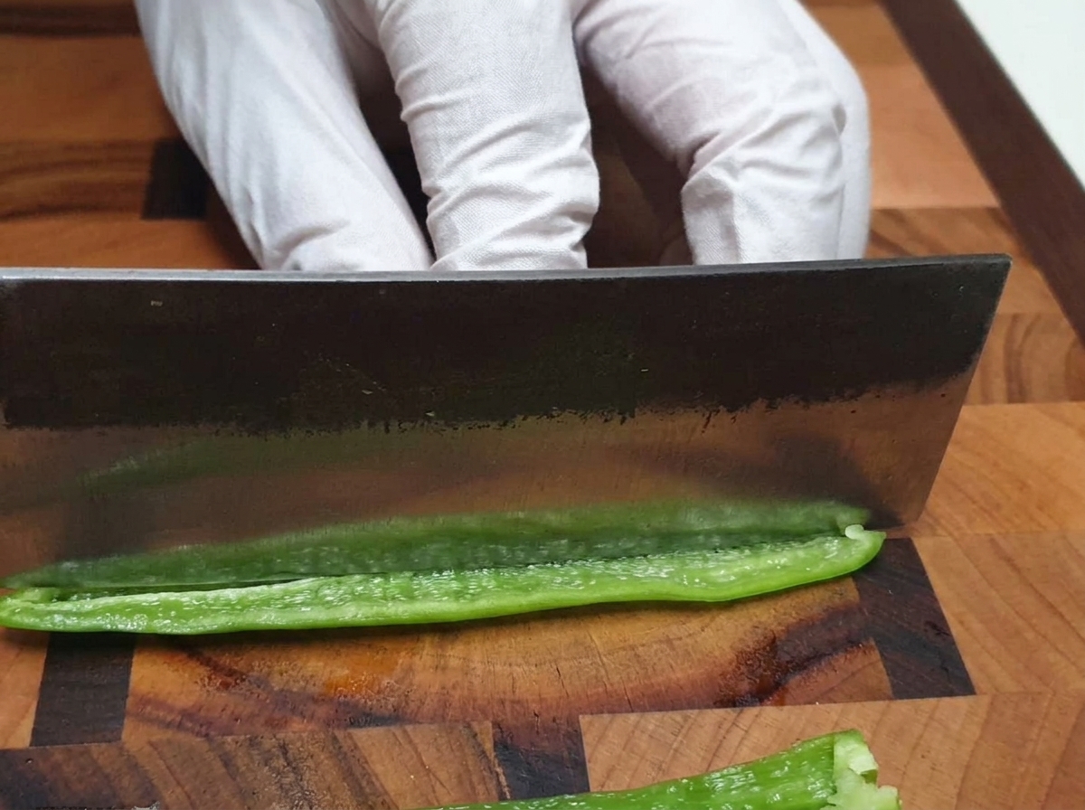 Un cuchillo de chef picando finamente un chile verde en una tabla de cortar de madera.
