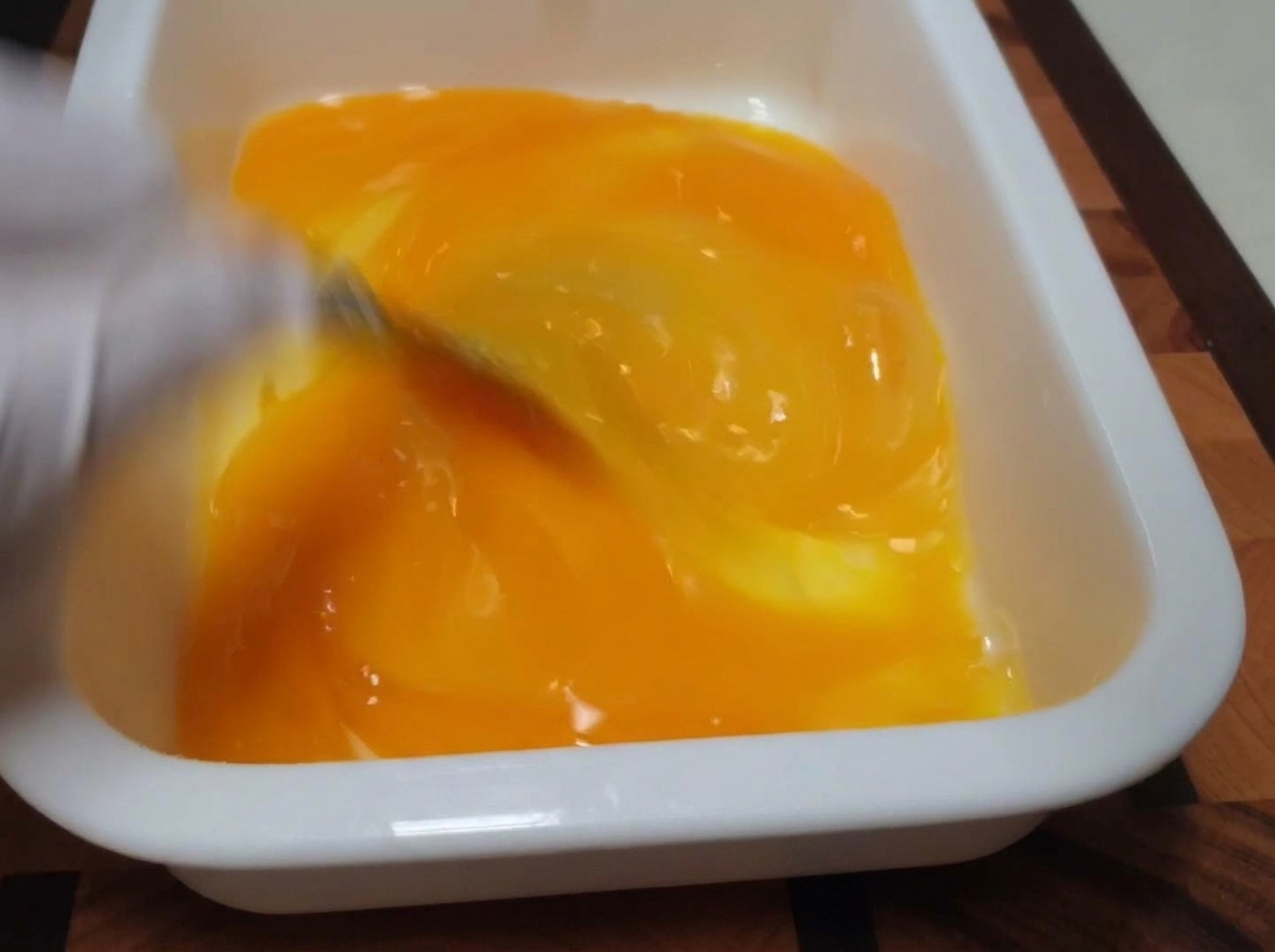 Unas varillas mezclando claras y yemas de color amarillo brillante en una bandeja rectangular blanca.